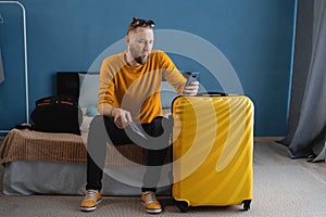 Man with suitcase checking out of hotel or home waiting for taxi ordered on mobile phone app. Air flight journey and