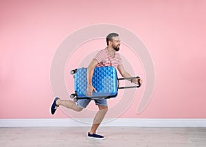 Man with suitcase running near color wall