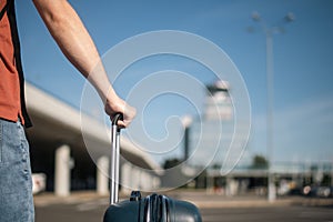 Man with suitcase is walking from parking lot to airport terminal