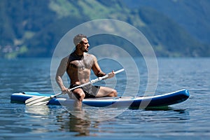 Man on Summer Alps lake. Strong muscular sexy man paddling on paddle board or sup. Summer vacation in Swiss. Summer