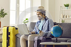 Man in summer hat using laptop for hotel booking or reservation from home