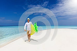 Man on summer holidays holding a yellow floaty walks down a beach