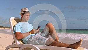 Man on summer vacation on the beach using phone