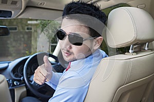 Man with sunglasses in the driving seat. Looking back and showing thumb up
