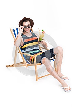 man in sunglasses and hat relaxing on beach chair with cocktail, isolated on white