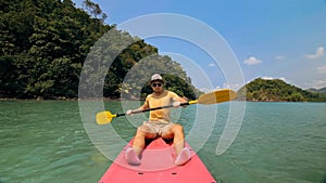 Man with sunglasses and hat rows pink plastic canoe along sea ag