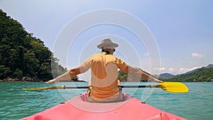 Man with sunglasses and hat rows pink plastic canoe along sea ag photo