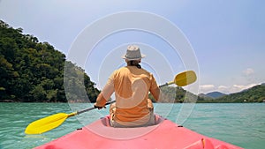 Man with sunglasses and hat rows pink plastic canoe along sea ag