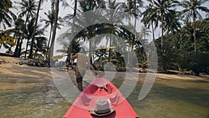 Man with sunglasses and hat rows pink plastic canoe along sea against green hilly islands with wild jungles. Traveling