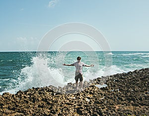 A man in sunglasses stands on the shore in the spray from the crashing waves photo