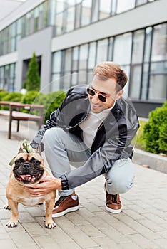 Man in sunglasses stroking french bulldog on street