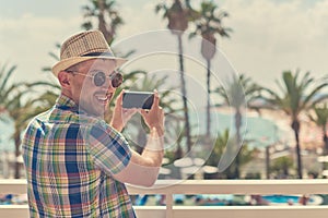 Man in sunhat looking in the camera while making photo of amazing sea photo