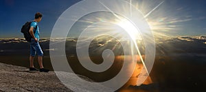 Man on sunshining rock above stormy clouds. Panorama