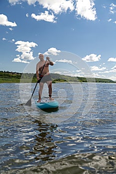 A man on a SUP board swims in a lake on a sunny day against a sky with clouds