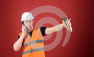 Man supervises construction on phone, red background. Supply of building materials concept. Engineer, architect on busy