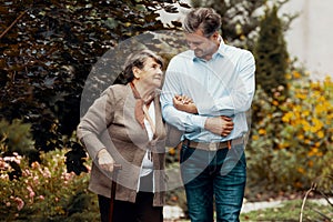 Man supporting weak senior woman with walking stick in the garden