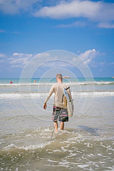 Man with surf board in ocean, rear view