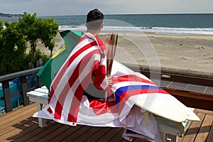 Man with Surfboard , and torch used in famous surf event and various flags around him.