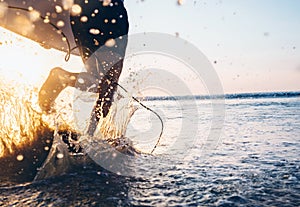 Man surfer run in ocean with surfboard. Closeup image water splashes and legs, sunset light