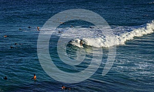 A man surfing on white foam wave in blue ocean with people swimming