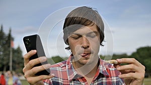 man surfs internet with phone eating pizza in green park