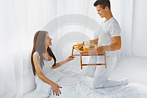 Man surprising woman with breakfast in bed