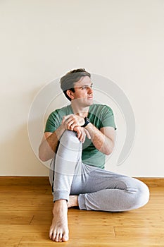 Man in sweatpants and a t-shirt sits on the floor leaning on a wall