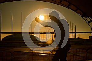 A man in a sweatshirt trains in boxing at the stadium at sunset. Athlete silhouette.