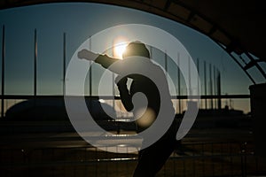A man in a sweatshirt trains in boxing at the stadium at sunset. Athlete silhouette.