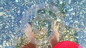 A man in swimming shorts walks in sea water. Multicolored sea stones under clear water on a pebble beach at night with