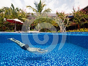 A man swimming underwater in pool in the tropical resort villa on a summer day.