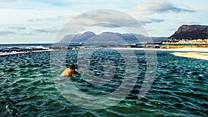 Man swimming in a wind-swept tidal pool against mountain backdrop.