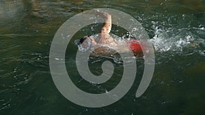 A man swims breaststroke in the river against the current