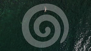 Man swims in the sea or ocean. Aerial view of guy floating swimming forward. The camera zooms down.