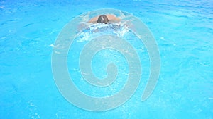 A man swims under the water in a pool with blue water. view from above.