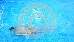A man swims under the water in a pool with blue water. View from above.