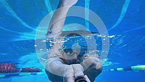 A man swims underwater in a pool and films himself on camera