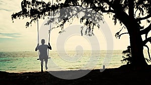 Man on Swing hang and tree on tropical beach. Summer holiday and vacation concept.