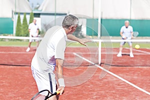 Man swinging racket while playing tennis doubles on red court during summer weekend