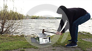 Man swings sledge hammer into printer, compuer and monitor on nature background with grasss, river, waves and sky
