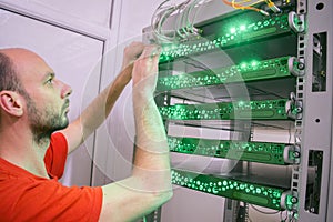 A man switches the wires in the computer equipment. Portrait of a technician in the server room of a data center. The technician