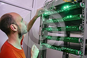 A man switches the wires in the computer equipment. Portrait of a technician in the server room of a data center. The technician