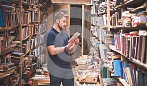 Man in a T-shirt and a beard stands in an old public library with a book in his hands