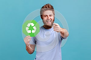 Man in T-shirt holding green recycling sign, saving environment, ecology concept, pointing to camera