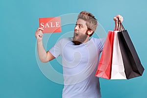 Man in T-shirt holding paper bags and looking at sale card, shopping and discounts, yelling happily