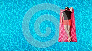 Man in t-shirt and shorts on inflatable mattress in the swimming pool.