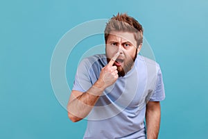 Man in T-shirt standing touching his nose, showing lie gesture, suspecting falsehood, dishonest talk