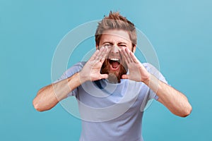 Man in T-shirt yelling widely opening mouth holding hands on face, screaming announcing his opinion.