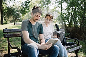 Man with tablet sitting on bench next to girl with camera