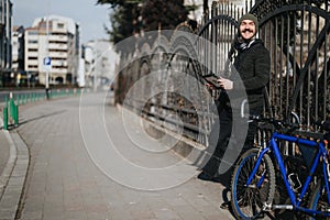 Man with a tablet smiling while resting on a bike in an urban setting